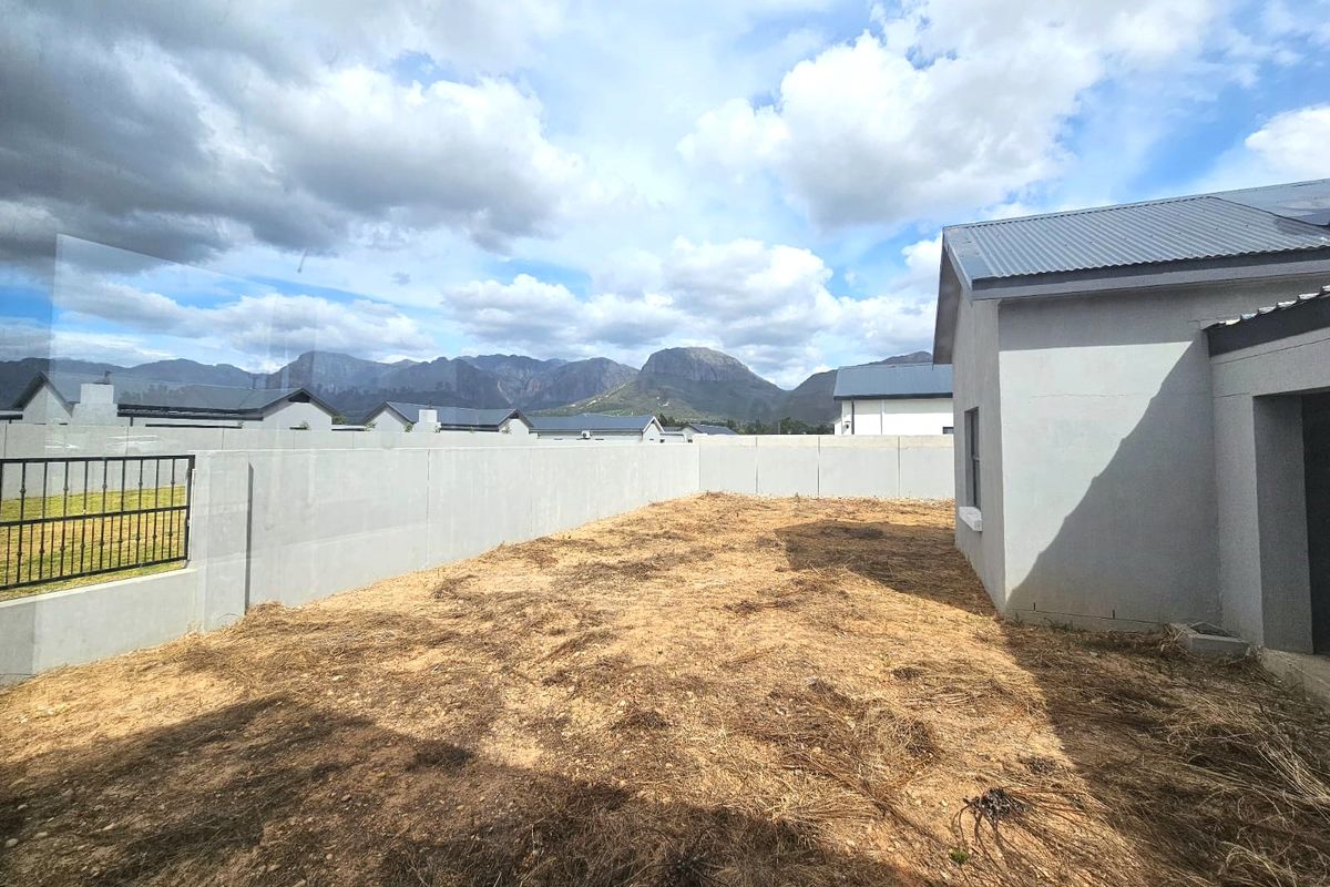Rear exterior view of the property featuring a large, unlandscaped garden area enclosed by concrete boundary walls with mountain views in the background.