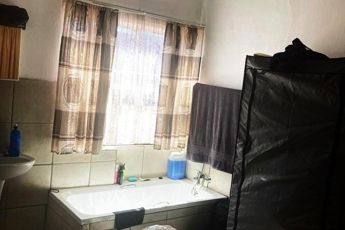 A functional bathroom featuring a built-in bathtub with tiled surround, wall-mounted basin, and window with privacy curtains.