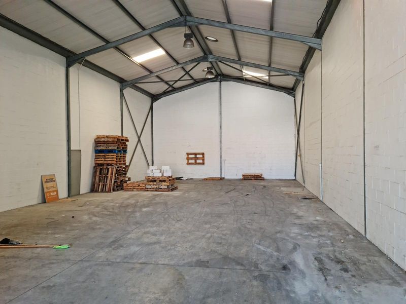Spacious industrial warehouse unit featuring exposed steel portal frame construction, concrete flooring, painted blockwork walls, and natural light provided by integrated skylights.