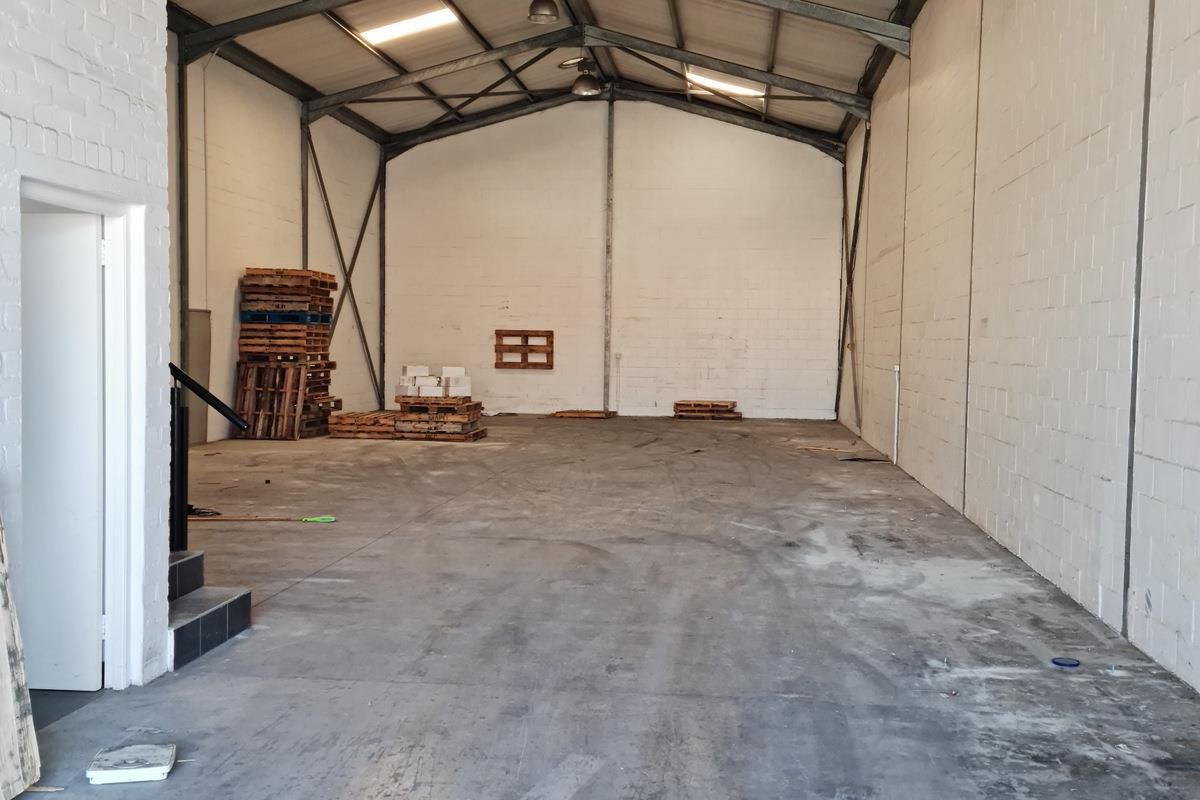 Spacious industrial warehouse or utility space featuring high ceilings with exposed steel trusses, concrete flooring, and durable painted brick walls.