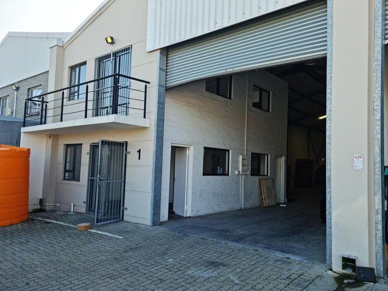 Commercial unit featuring a large roller shutter door, a first-floor balcony with metal railing, and paved exterior access.