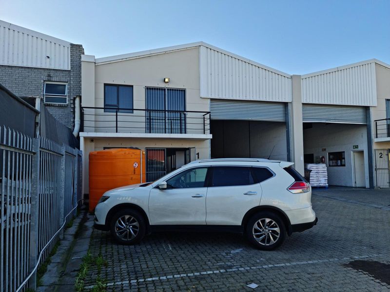 Front elevation of a commercial industrial unit featuring roller shutter doors, a small balcony, and paved parking area.