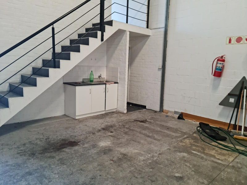 Industrial utility space featuring a staircase, kitchenette area with sink, and exposed brick walls, suitable for storage or workshop use.