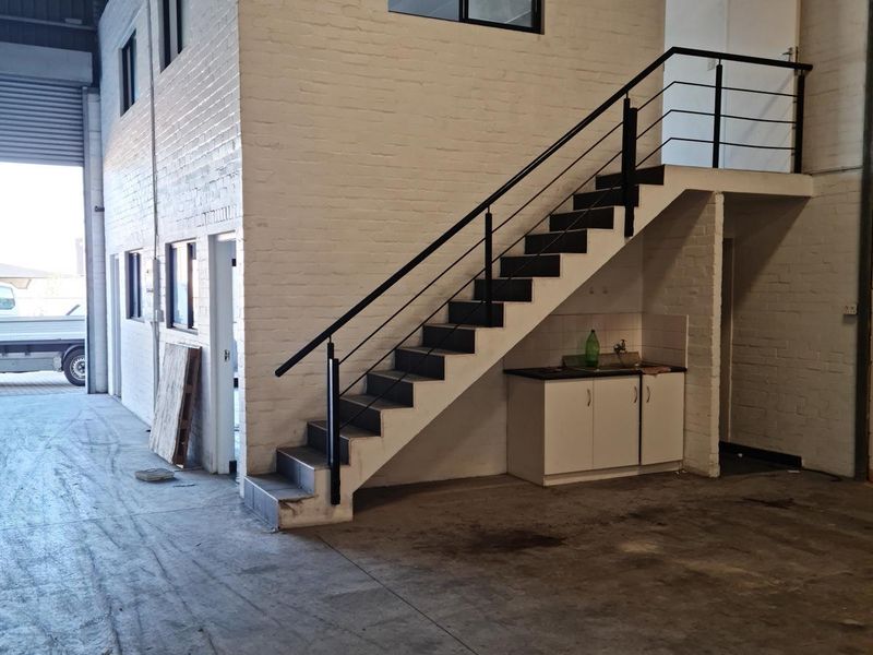 Commercial warehouse space featuring a mezzanine level, metal staircase, built-in kitchenette, and large roller shutter door access.