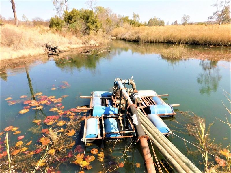 A floating water pump system installed on a farm dam, featuring integrated piping and infrastructure for irrigation purposes.
