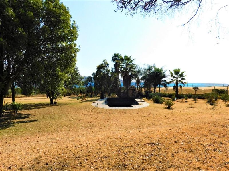 A wide view of a farm property featuring a swimming pool set within a large, dry garden area with mature trees.