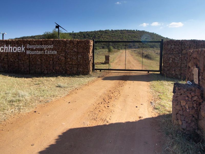 Entrance to Boschhoek Mountain Estate featuring a secure gate, gabion stone walls, and a dirt access road leading into the property.