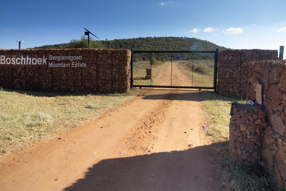 Entrance to Boschhoek Mountain Estate featuring a secure gate, gabion stone walls, and a dirt access road leading into the property.