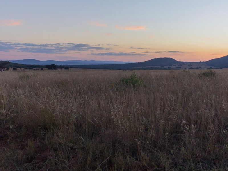 A scenic view of expansive, undeveloped commercial land featuring natural grasslands and distant mountain ranges at sunset.