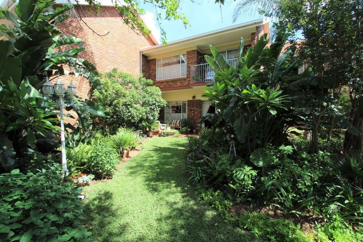 A view of the rear exterior of the apartment building, featuring a lush garden, lawn, and a balcony with metal railings.