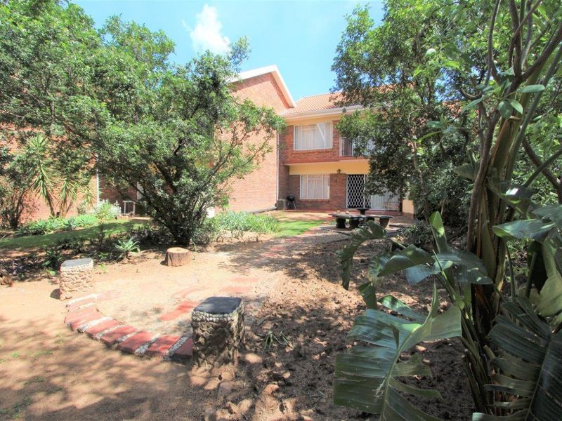 Rear view of the apartment building featuring a brick facade, tiled roof, and a private garden area with a paved pathway.