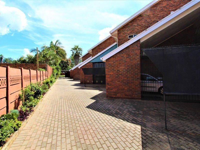 Exterior view of the apartment complex featuring a paved driveway, brick facade, and covered parking areas.