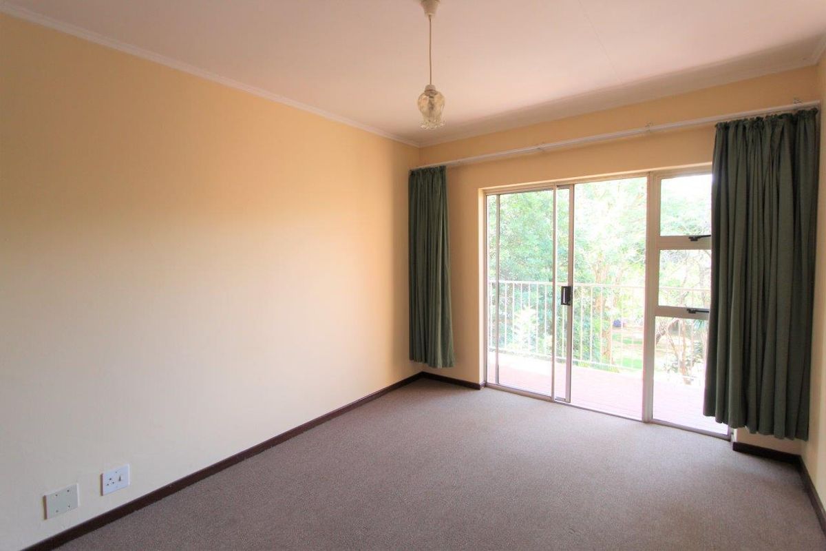 A spacious, empty bedroom featuring neutral walls, carpeted flooring, and a sliding glass door providing access to an outdoor balcony area.