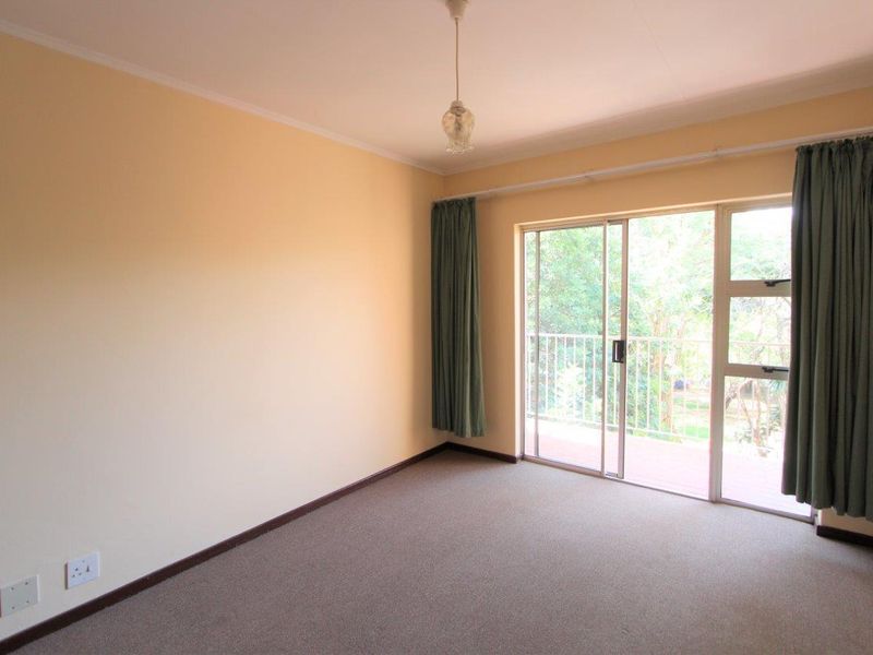 A spacious, empty bedroom featuring neutral walls, carpeted flooring, and a sliding glass door providing access to an outdoor balcony area.