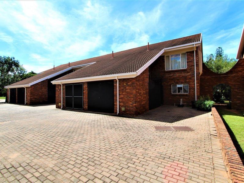Front exterior view of a brick apartment complex featuring a paved driveway, tiled roof, and secure garage access.