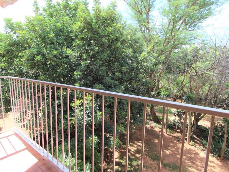 A private balcony featuring a metal balustrade and tiled flooring, offering a peaceful view of the surrounding mature trees and garden area.