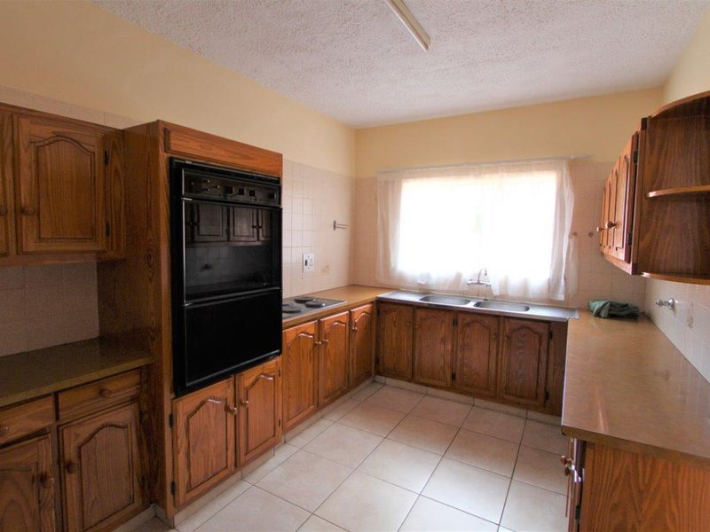 A dated kitchen featuring wooden cabinetry, built-in oven, hob, and double sink with tiled flooring and backsplash.