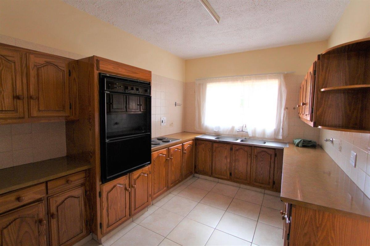A dated kitchen featuring wooden cabinetry, built-in oven, hob, and double sink with tiled flooring and backsplash.