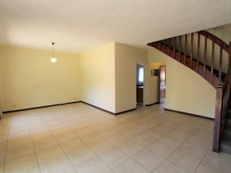 Spacious open-plan living area featuring tiled flooring and a traditional wooden staircase, offering a blank canvas for interior design updates.