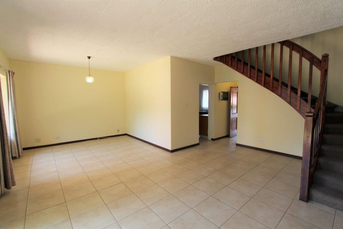 Spacious open-plan living area featuring tiled flooring and a traditional wooden staircase, offering a blank canvas for interior design updates.
