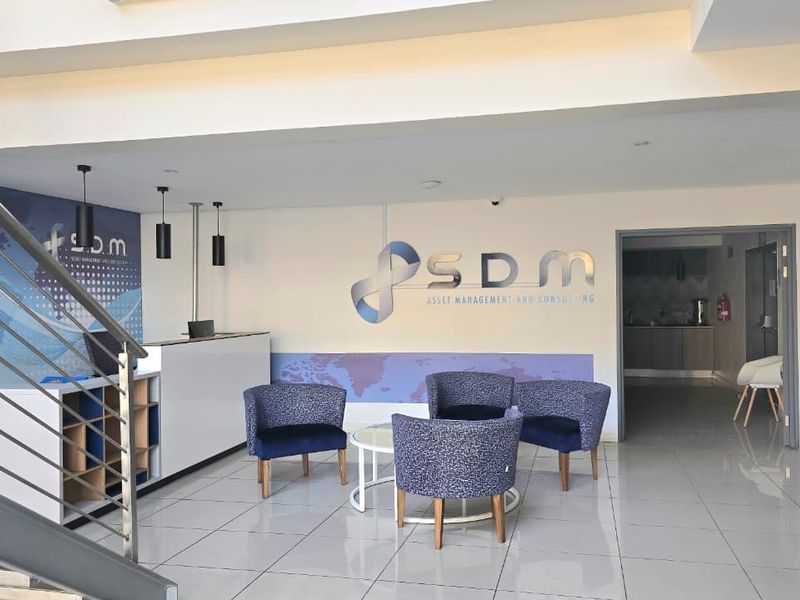 Professional office reception area featuring a branded wall, tiled flooring, built-in reception desk, and staircase access.