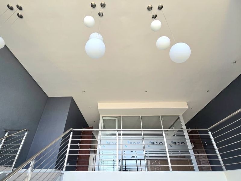 Modern office interior featuring a glass partition wall, stainless steel balustrade, and contemporary pendant lighting in a bright, open-plan workspace.
