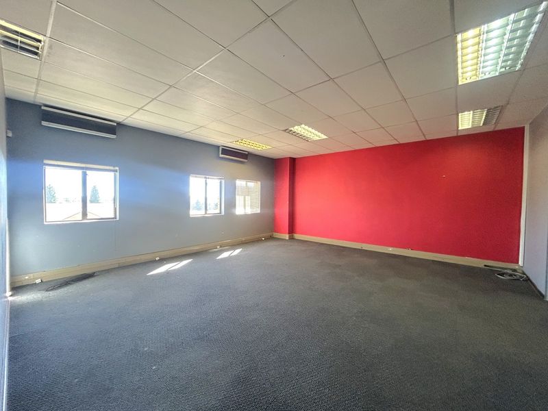 An empty, open-plan office space featuring a suspended ceiling, recessed lighting, wall-mounted air conditioning units, and carpeted flooring.