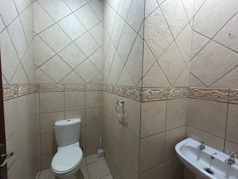 A compact bathroom featuring full-height tiled walls with decorative border detailing, a standard toilet, and a pedestal basin.