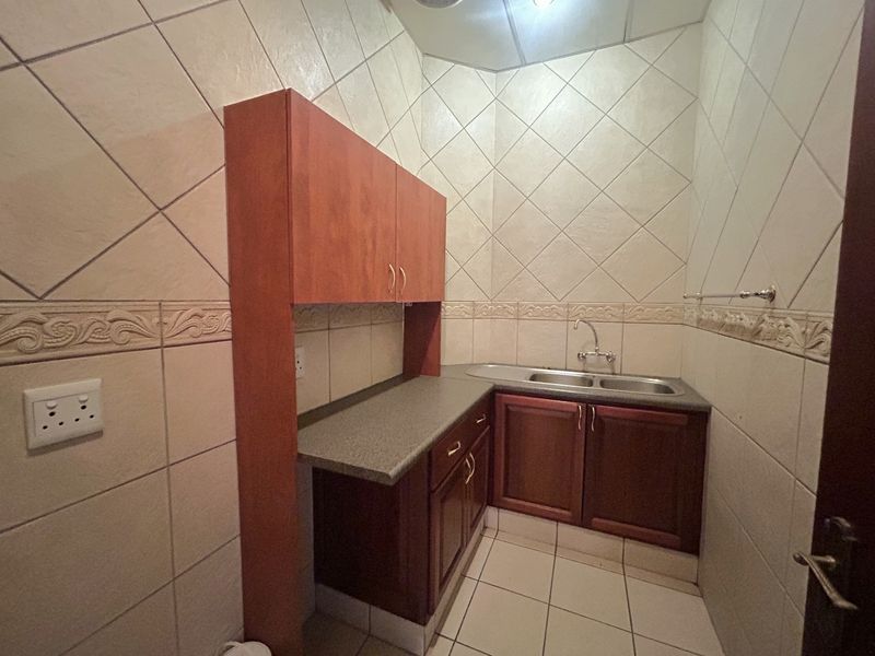A compact scullery or kitchenette area featuring built-in wooden cabinetry, a double basin sink, and tiled finishes throughout.