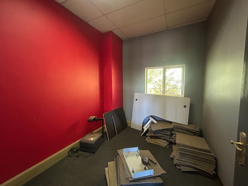 A vacant office space featuring a suspended ceiling, carpeted flooring, and a window with blinds, currently used for storage of loose materials.