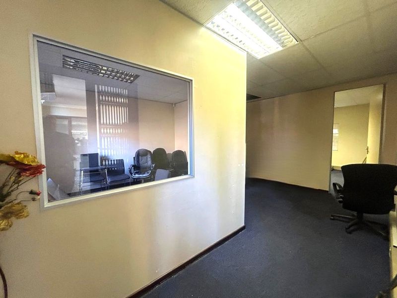 Office space featuring an internal glass partition, fluorescent lighting, and carpeted flooring, offering a functional layout for a professional work environment.