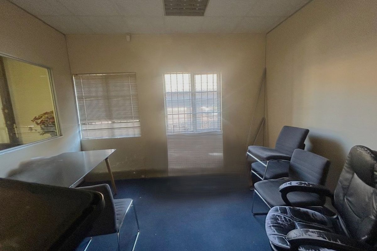 A dated office space featuring a suspended ceiling, recessed lighting, and window blinds, currently requiring cosmetic updates to the flooring and wall finishes.
