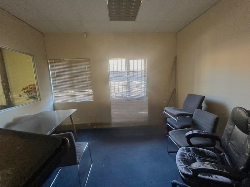 A dated office space featuring a suspended ceiling, recessed lighting, and window blinds, currently requiring cosmetic updates to the flooring and wall finishes.