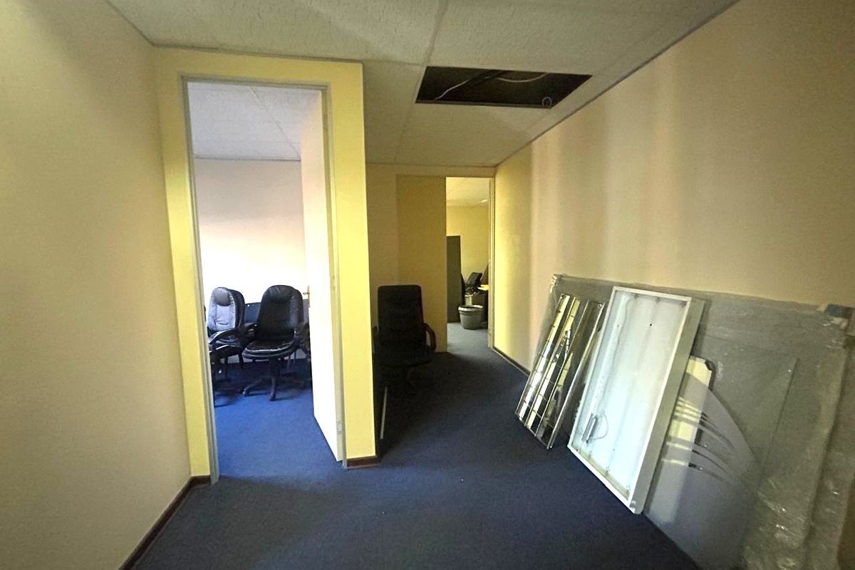 Office corridor area featuring blue carpeting and a suspended ceiling with a missing tile, requiring maintenance and cosmetic updates.
