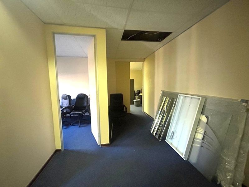 Office corridor area featuring blue carpeting and a suspended ceiling with a missing tile, requiring maintenance and cosmetic updates.