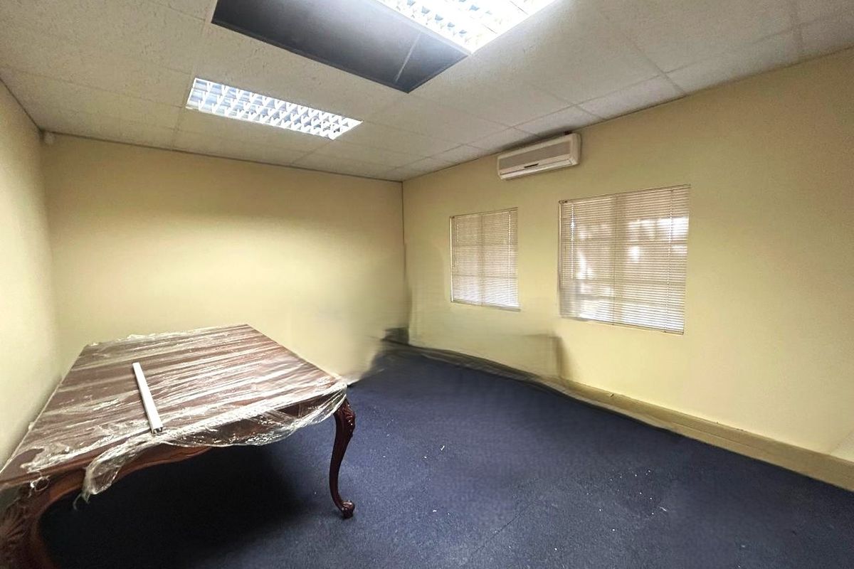 An empty office space featuring a suspended ceiling with recessed lighting, wall-mounted air conditioning, and carpeted flooring.