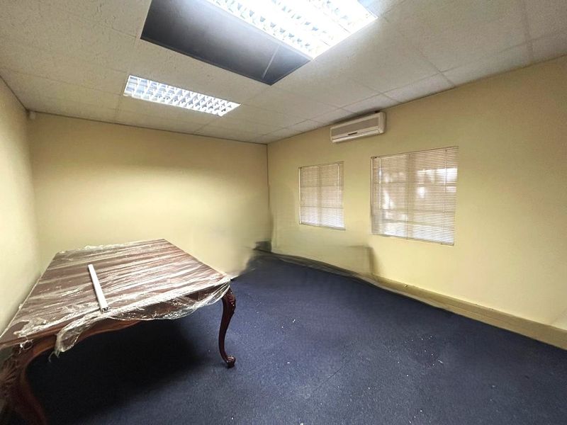 An empty office space featuring a suspended ceiling with recessed lighting, wall-mounted air conditioning, and carpeted flooring.