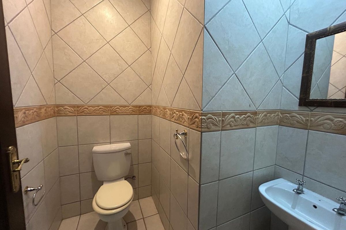 A compact office bathroom featuring full-height tiled walls with decorative border, a pedestal sink, and a standard toilet.
