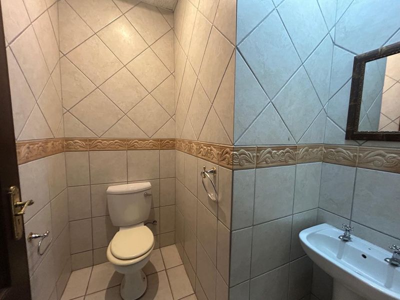 A compact office bathroom featuring full-height tiled walls with decorative border, a pedestal sink, and a standard toilet.