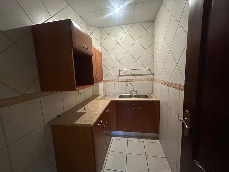 A compact scullery or kitchenette area featuring built-in wooden cabinetry, a double bowl sink, and full-height wall tiling.