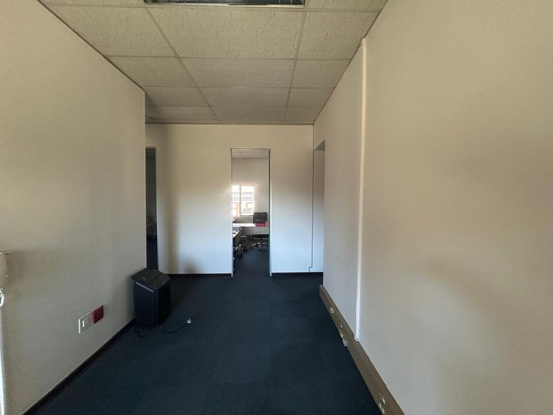 A vacant office hallway featuring a suspended ceiling, dark carpeting, and access to adjacent office spaces.