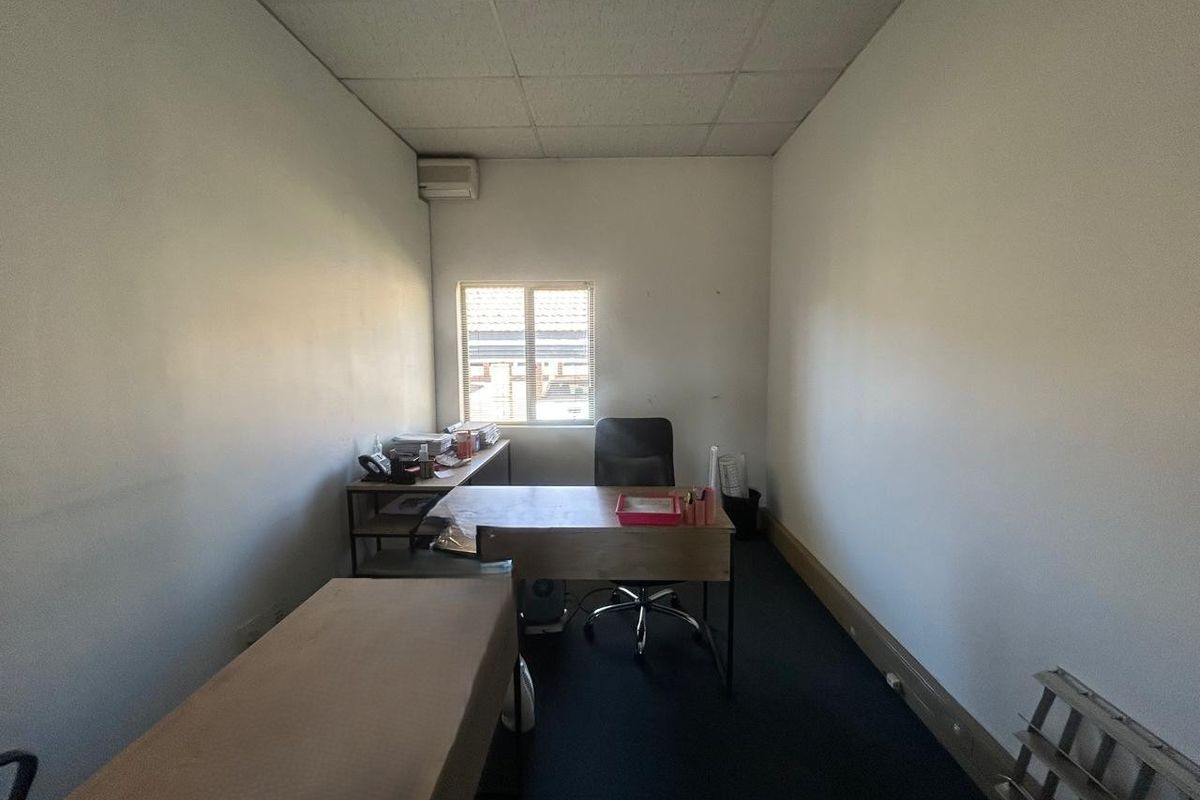 A functional office space featuring a suspended ceiling, wall-mounted air conditioning unit, and carpeted flooring, providing a practical work environment.
