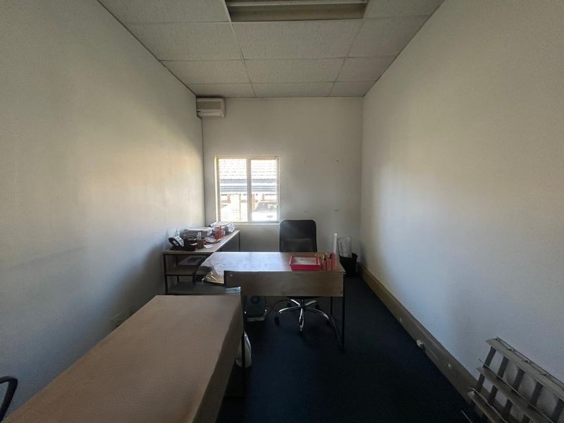 A functional office space featuring a suspended ceiling, wall-mounted air conditioning unit, and carpeted flooring, providing a practical work environment.