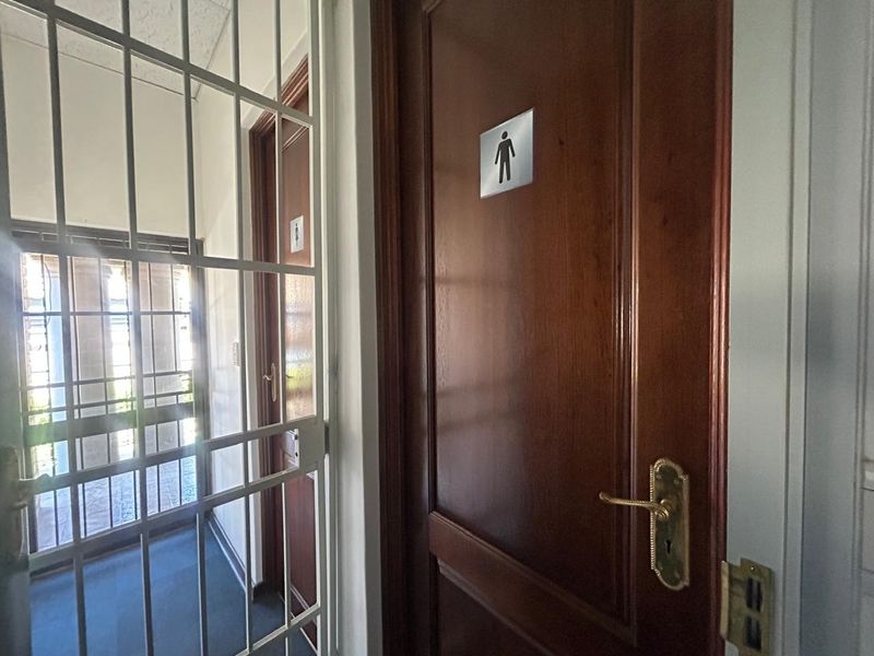 A hallway area featuring solid wood doors with brass hardware and a security gate, providing access to restroom facilities.