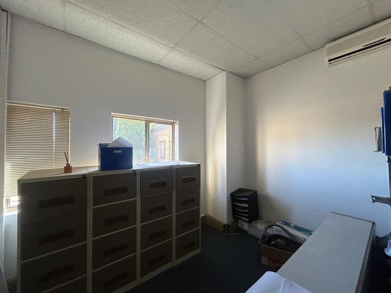 A functional office space featuring a suspended ceiling, split-system air conditioning, and windows fitted with venetian blinds.