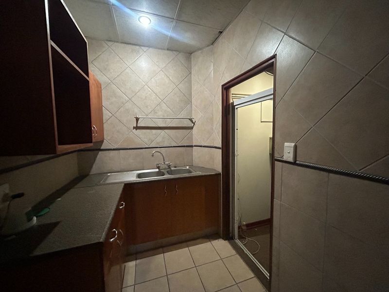 A small kitchenette area featuring built-in cabinetry, a double sink, and tiled finishes, currently requiring maintenance and repairs to the ceiling and doorway.