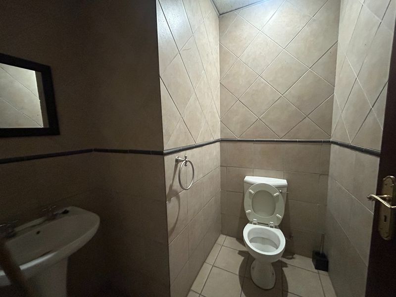 A compact office bathroom featuring a pedestal sink, toilet, and full-height wall tiling.