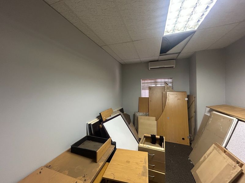 A small office space featuring a suspended ceiling with recessed lighting and a wall-mounted air conditioning unit, currently used for storage.