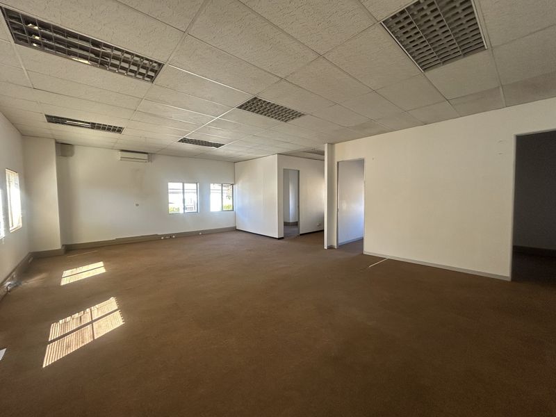 A spacious, empty open-plan office area featuring a suspended ceiling, recessed lighting, and wall-mounted air conditioning.
