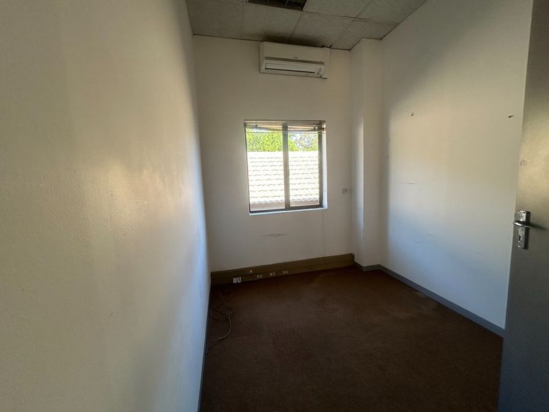 A vacant office space featuring carpet flooring, a wall-mounted air conditioning unit, and a window with blinds, ready for professional fit-out.
